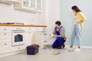 woman watching a plumber repair a kitchen pipe